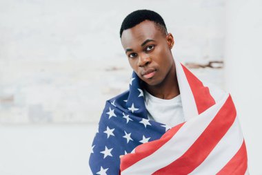 Amerikan bayrağıyla kaplanmış Afro-Amerikan adam kameraya bakıyor.