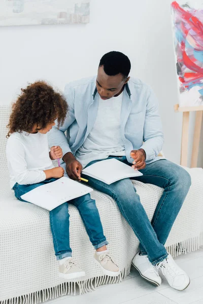 African American Father Daughter Holding Color Pencil While Sitting Sofa — Stock Photo, Image