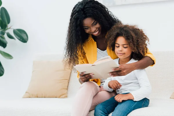 Afrikansk Amerikansk Mor Läser Bok Medan Sitter Med Dotter Soffan — Stockfoto