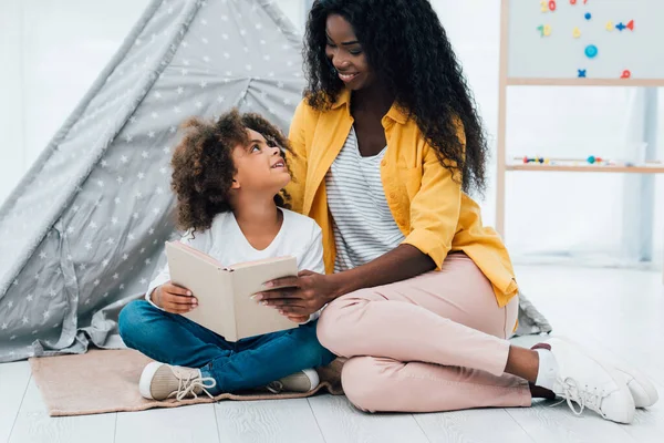 African American Kid Sitting Floor Holding Book Looking Brunette Mother — Stock Photo, Image