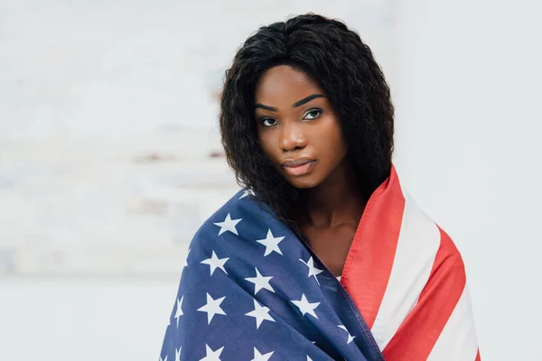 african american woman covered with flag of american looking at camera