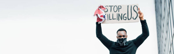 horizontal crop of african american man holding flag of america and placard with stop killing us lettering outside 