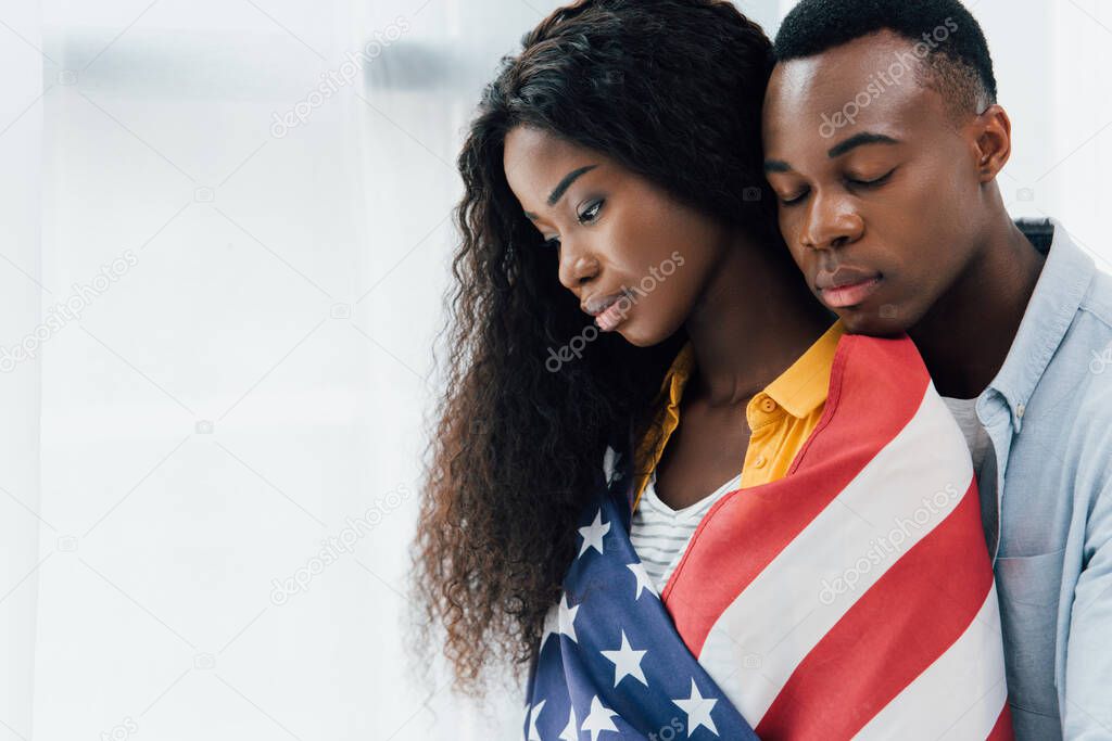 african american man with closed eyes near brunette woman covered with flag of america 