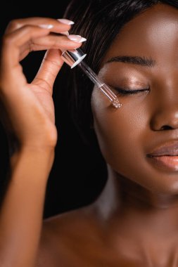 portrait of african american naked woman applying serum on face isolated on black clipart