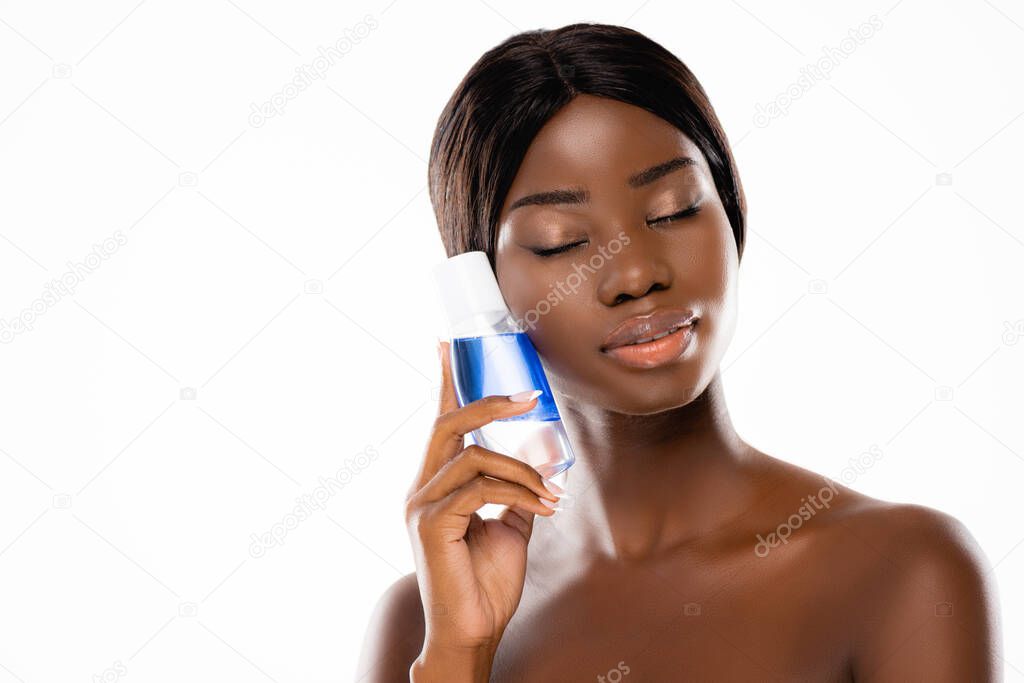 african american naked woman with closed eyes holding micellar water isolated on white