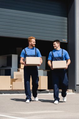 Şehir caddesinde karton kutular tutarken tulumlu hamallar birbirine bakıyor. 