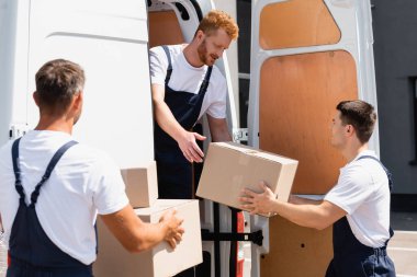 Şehir caddesinde kamyondan paketleri indirirken karton kutuyu meslektaşına veren yükleyicinin seçici odak noktası 