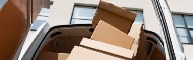 Panoramic shot of cardboard boxes in truck with open doors on urban street  clipart