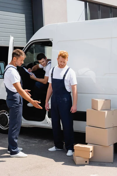 Geliefden Overalls Kijken Naar Kartonnen Dozen Buurt Van Collega Vrachtwagen — Stockfoto