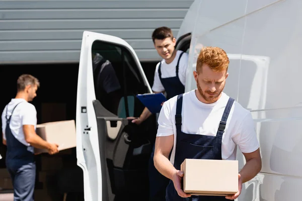 Selective Focus Loader Holding Cardboard Box While Colleagues Working Truck — Stock Photo, Image