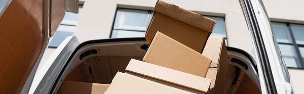 Panoramic shot of cardboard boxes in truck with open doors on urban street 