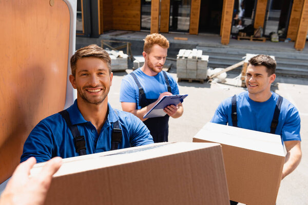 Selective focus of loader giving cardboard box to colleague in truck on urban street 