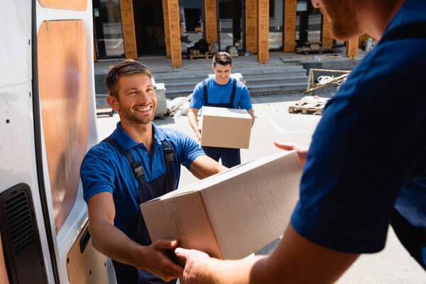 Selective focus of loader giving carton box to colleague in truck on urban street 