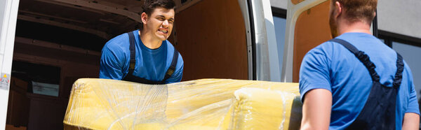 Panoramic orientation of movers unloading couch in stretch wrap in truck outdoors 