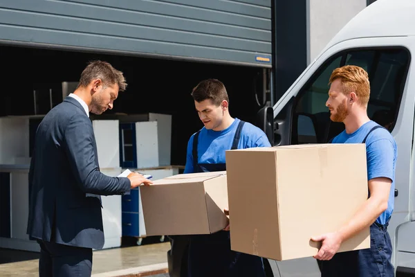 Empresário Com Prancheta Verificando Caixa Papelão Perto Movers Caminhão Livre — Fotografia de Stock