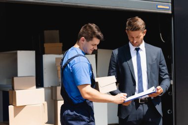 İş adamı ve deponun yanındaki panoda karton kutu yazılı üniformalı yükleyici. 