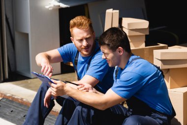 Yükleyici, dışarıdaki depodaki panoya bakan meslektaşına bakıyor. 