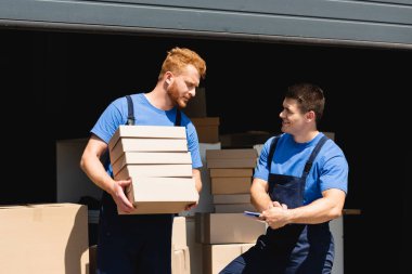 Depoda karton kutularla iş arkadaşına bakan bir dosya yükleyici. 