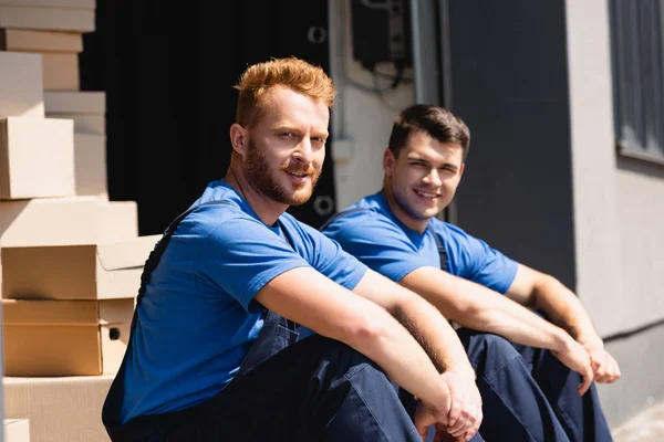 Nakliyecinin seçici odak noktası açık hava deposundaki iş arkadaşının yanındaki kameraya bakmak. 