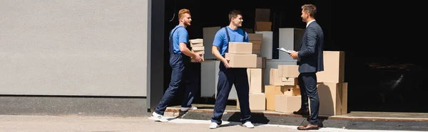 Panoramic Shot Movers Holding Cardboard Boxes Businessman Clipboard Warehouse Outdoors — Stock Photo, Image