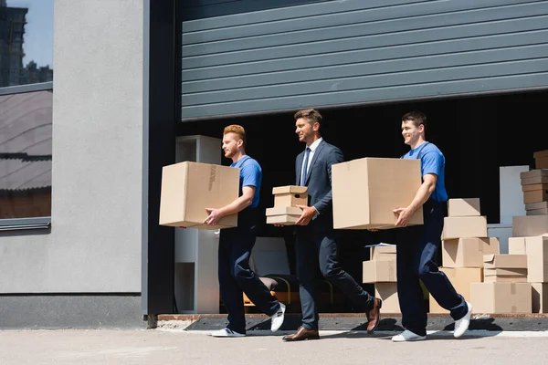 Empresário Segurando Caixas Papelão Enquanto Caminha Com Movers Rua Urbana — Fotografia de Stock