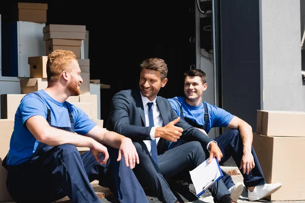 Depodaki karton kutuların ve nakliyecilerin yanında jest yaptığını gösteren panosu olan bir iş adamı. 