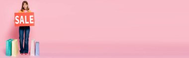 Pembe arka planda alışveriş çantalarının yanında satılık mektupları olan bir kadın kartı taşıması konsepti
