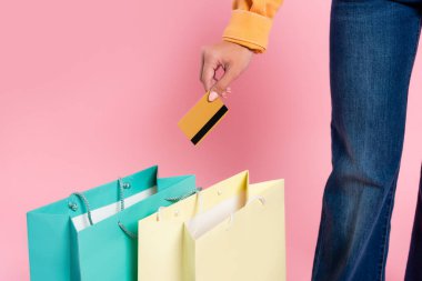 Pembe arka planda alışveriş torbalarının yanında kredi kartı tutan bir kadın görüntüsü.