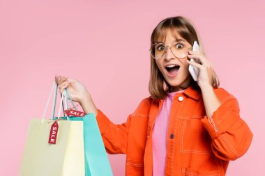 Güneş gözlüklü bir kadının elinde satış sözcüğüyle pembe arka planda akıllı telefondan konuşmasına şaşırdım.