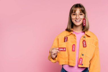 Pembe arka planda satılık harflerle fiyat etiketi gösteren genç bir kadın.