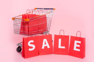 Pembe arka planda alışveriş arabasının yanındaki kırmızı alışveriş torbalarında mektup satışı.