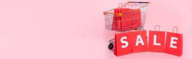 Pembe yüzeydeki alışveriş arabasının yanındaki kırmızı alışveriş çantalarında panoramik kelime satışı kavramı
