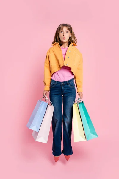 提着购物袋跳到粉色背景上的震惊女人 — 图库照片