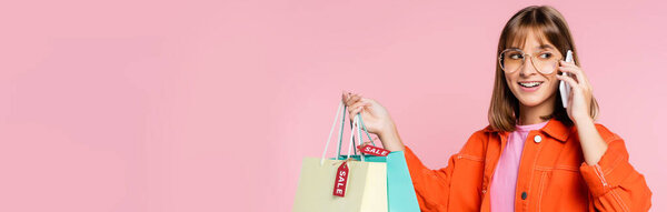 Горизонтальная концепция женщины разговаривающей на смартфоне и держащей сумки с ценниками, изолированными на розовом 