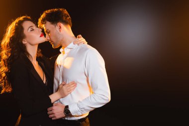 Ceketli kıvırcık kadın siyah gömlekli adama sarılıyor. 