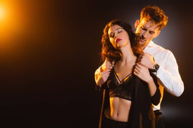Takım elbiseli adam siyah gözleri kapalı seksi kadına ceketini çıkarıyor. 