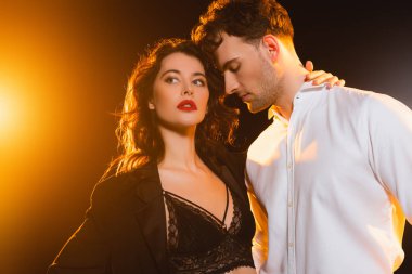 Gömlekli bir adam dantelli sutyen ve siyah ceketli kıvırcık bir kadına bakıyor. 