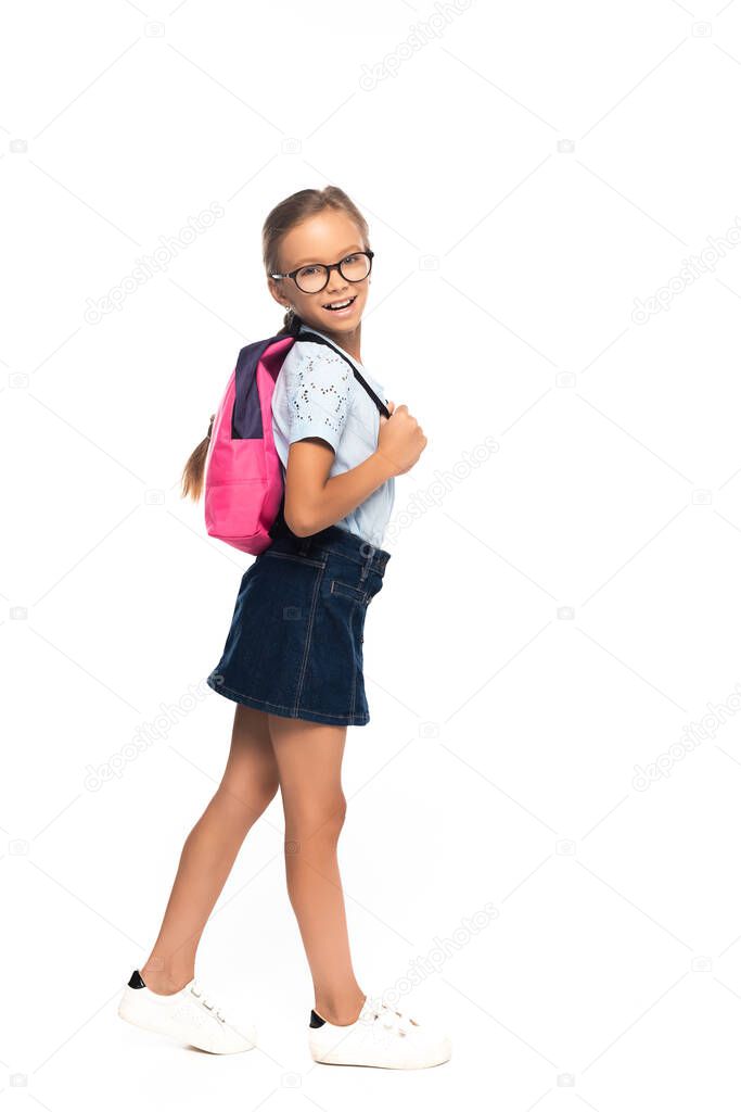 schoolgirl in glasses standing and touching backpack isolated on white 