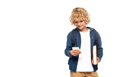 Sarışın ve kıvırcık okul çocuğu kitap tutuyor ve beyaz üzerine izole akıllı telefon kullanıyor. 