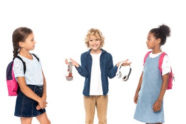 blonde schoolboy holding wireless headphones near multicultural schoolgirls isolated on white  clipart