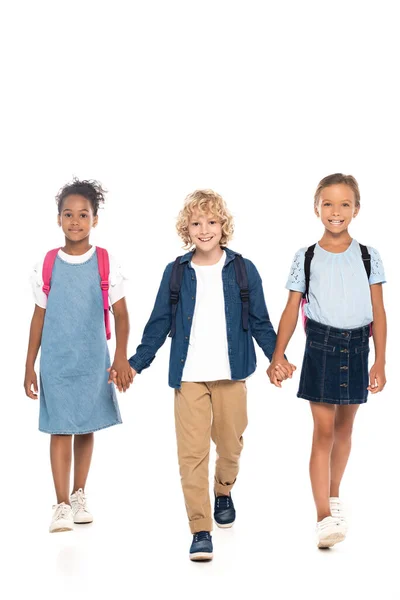 Blondýny Kudrnatý Školák Drží Ruce Multikulturní Školačky Při Chůzi Izolované — Stock fotografie