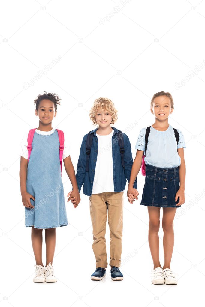 blonde schoolboy holding hands with multicultural schoolgirls isolated on white 