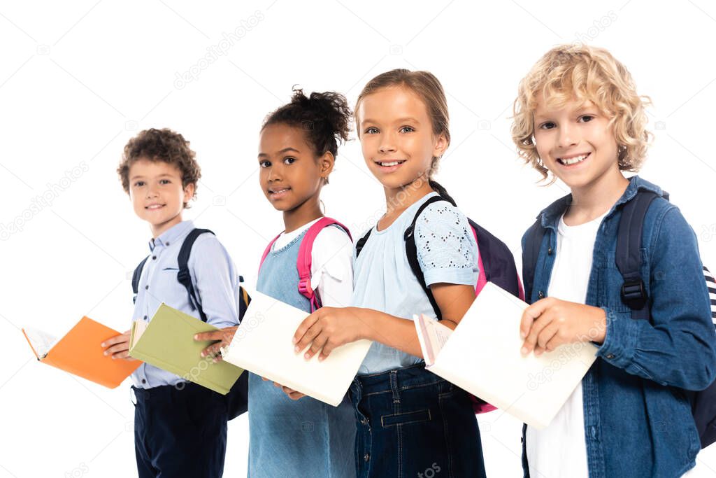 selective focus of multicultural schoolchildren with backpacks holding books isolated on white 