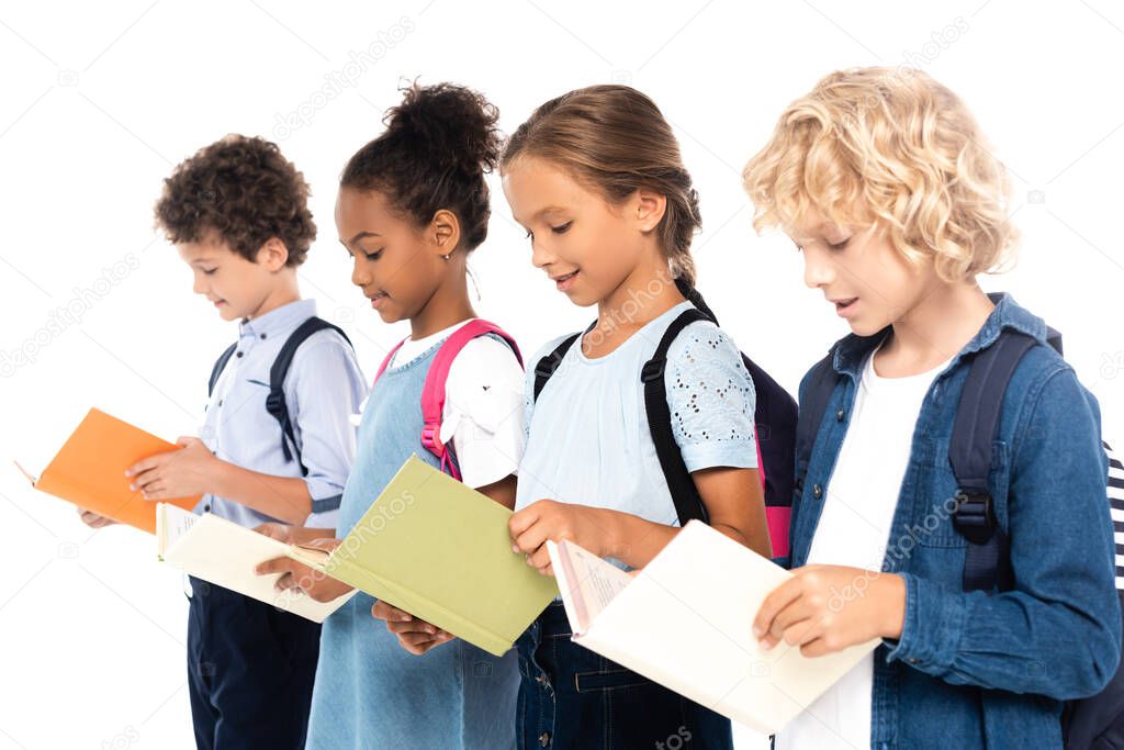 selective focus of multicultural schoolchildren with backpacks reading books isolated on white 