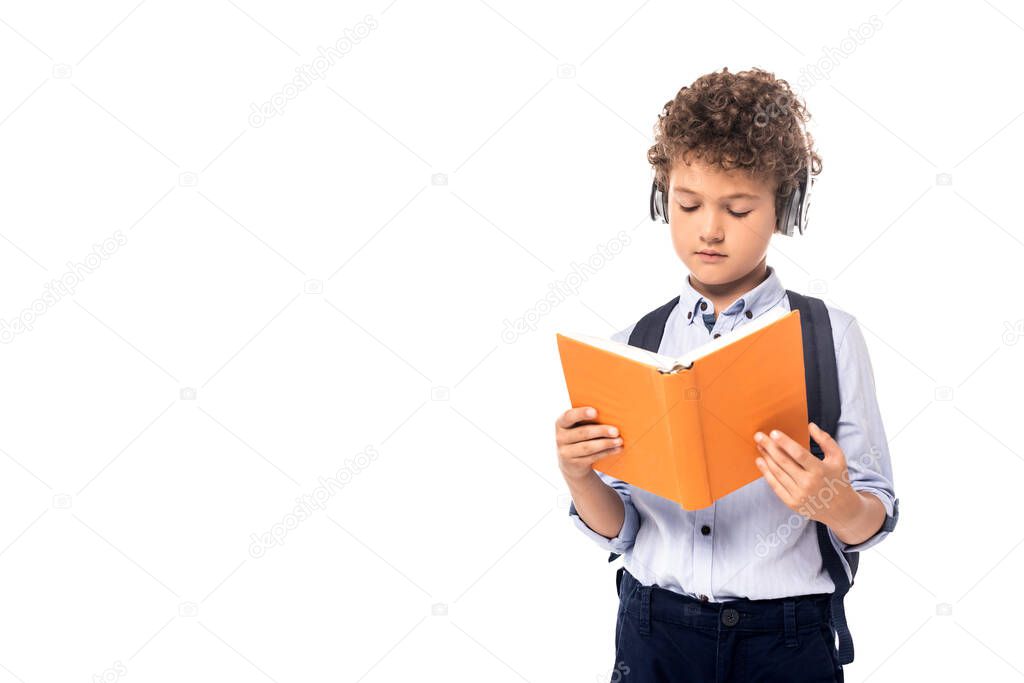curly schoolboy in wireless headphones reading book isolated on white 
