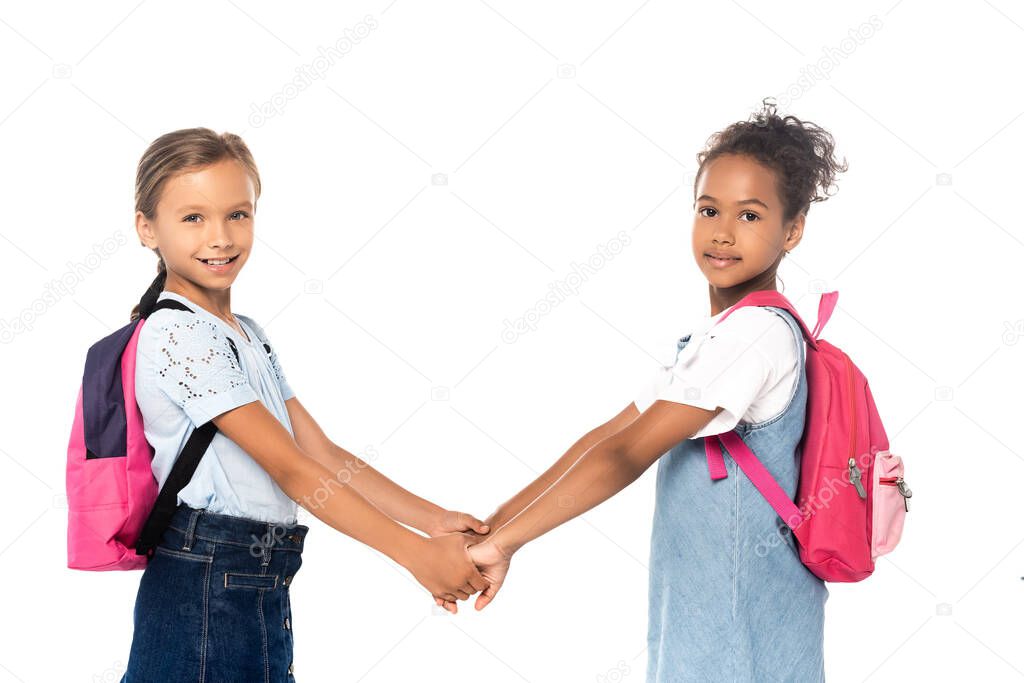 multicultural schoolkids holding hands and looking at camera isolated on white 