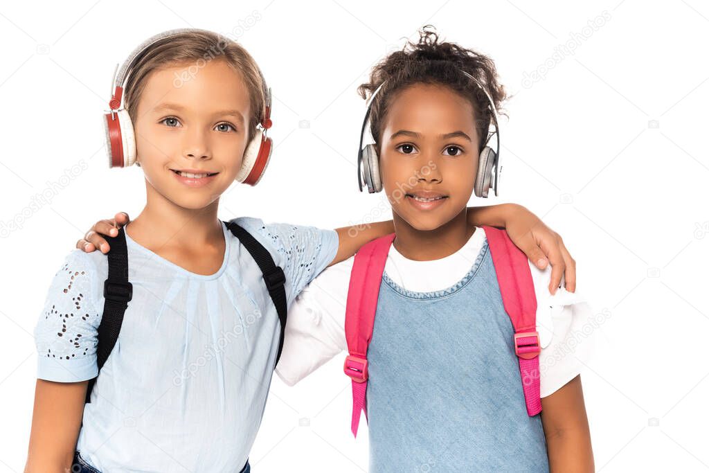 multicultural schoolkids listening music in wireless headphones while looking at camera isolated on white 