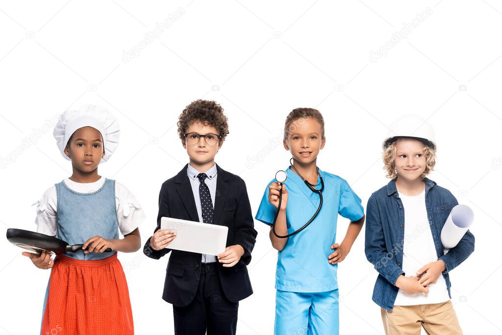 multicultural children in costumes of different professions holding blueprint, frying pan, stethoscope and digital tablet isolated on white 