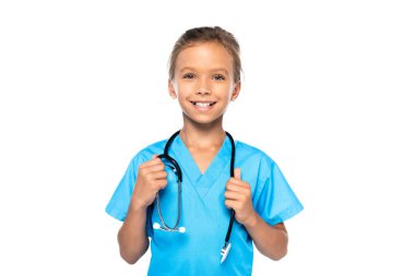 Doktor kostümlü çocuk steteskopa dokunuyor ve beyaz kameraya bakıyor. 