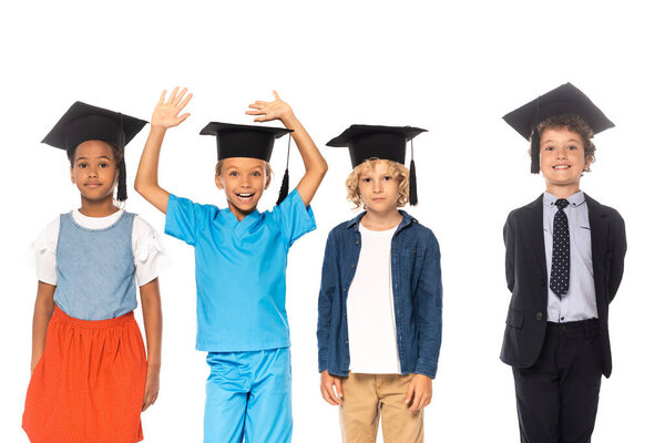 мультикультурные дети в выпускных шапках, одетые в костюмы разных профессий, стоят рядом с ребенком с поднятыми руками, изолированными на белом 